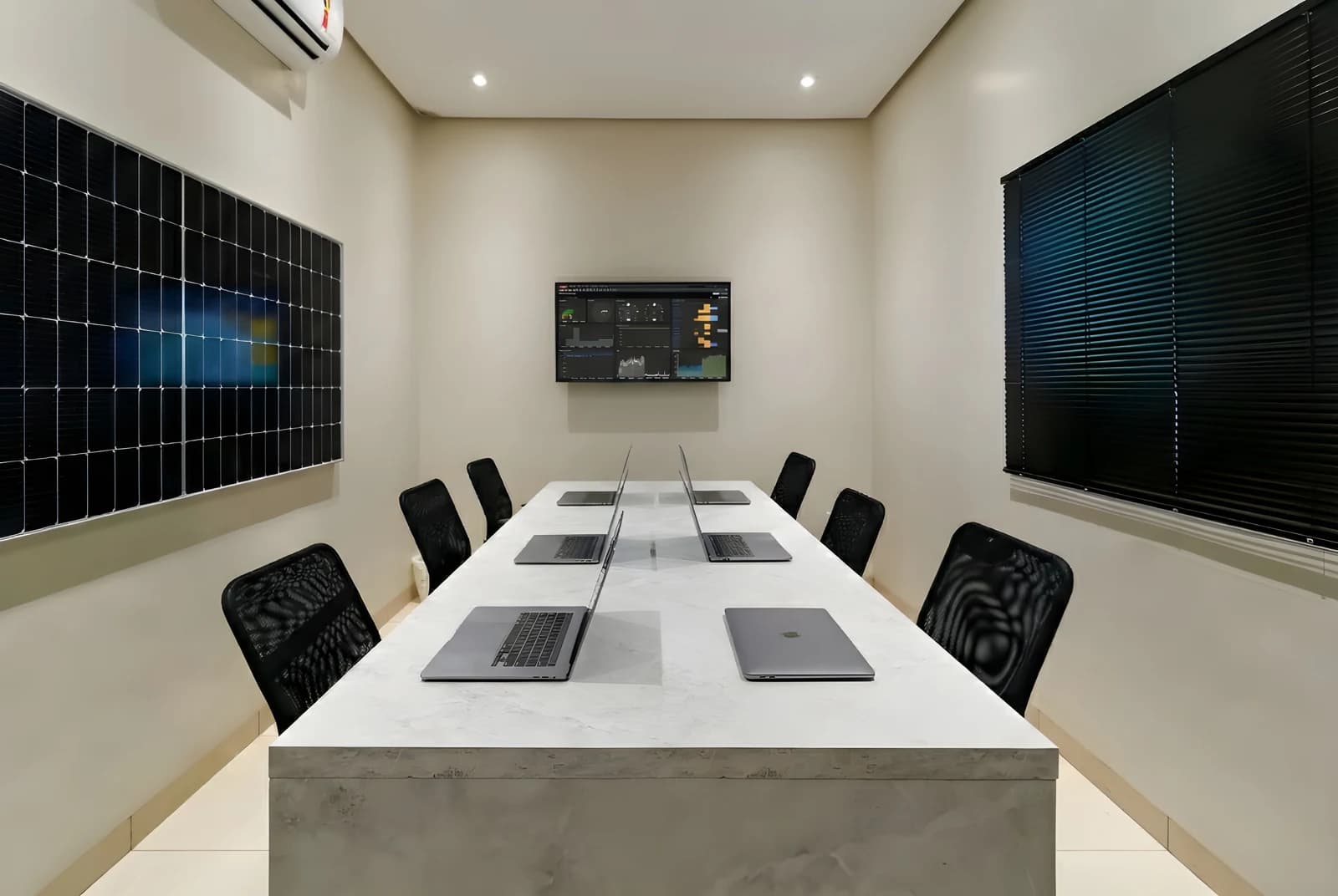 Sala de reuniões com mesa em MDF Pietra Santa, cadeiras pretas, persiana escura e tela na parede.
