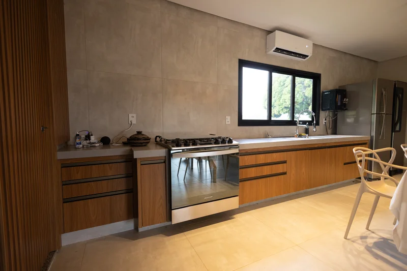 Cozinha de fazenda com armários em MDF Louro freijó, Portas Roma em alumínio bronze e bancada clara sob luz natural.