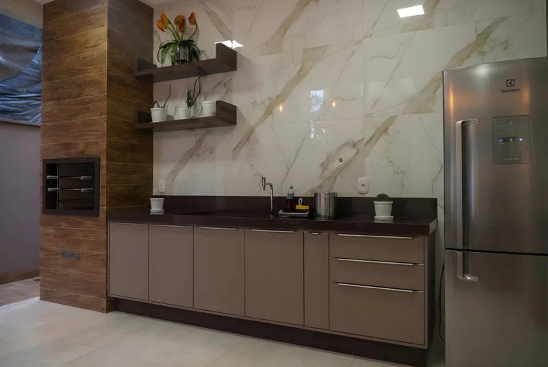 Bancada com pedra Café, MDF Chocolat Light e portas Versatile champagne em churrasqueira gourmet com iluminação suave.