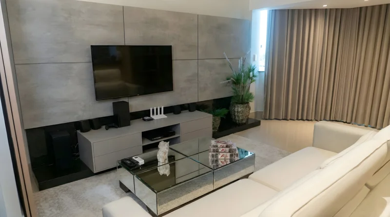 Sala de TV com painel em MDF Santorini, base Preto Málaga e faixa em Espelho Cristal, com TV e cortinas claras.