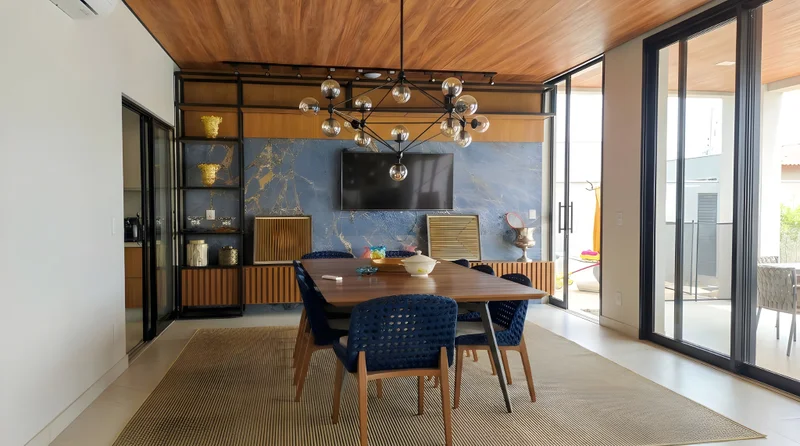 Varanda gourmet com painel em Louro Freijó ripado, pedra Mar Dourado e estrutura metálica preto fosco.